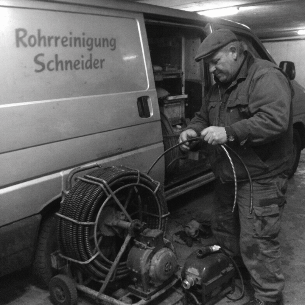 Fachkraft öffnet im Keller eines Mehrfamilienhauses eine Revisionsklappe und legt das Werkzeug bereit